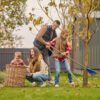 Moderne familietuin met speelgazon, ingegraven trampoline, pergola en stijlvolle loungehoek voor kinderen en volwassenen.